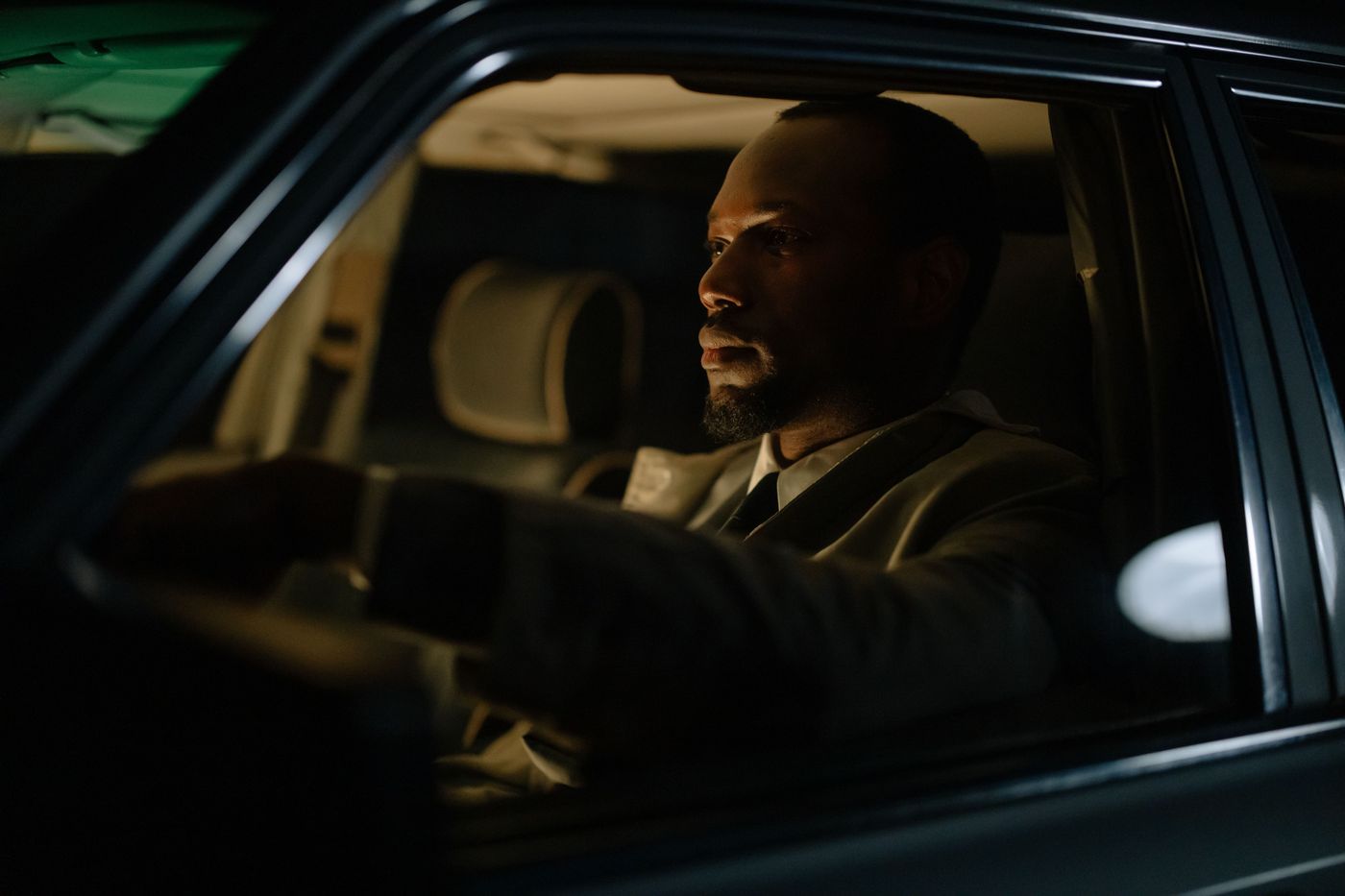 A chauffeur in a suit at the wheel of a dark cabin
