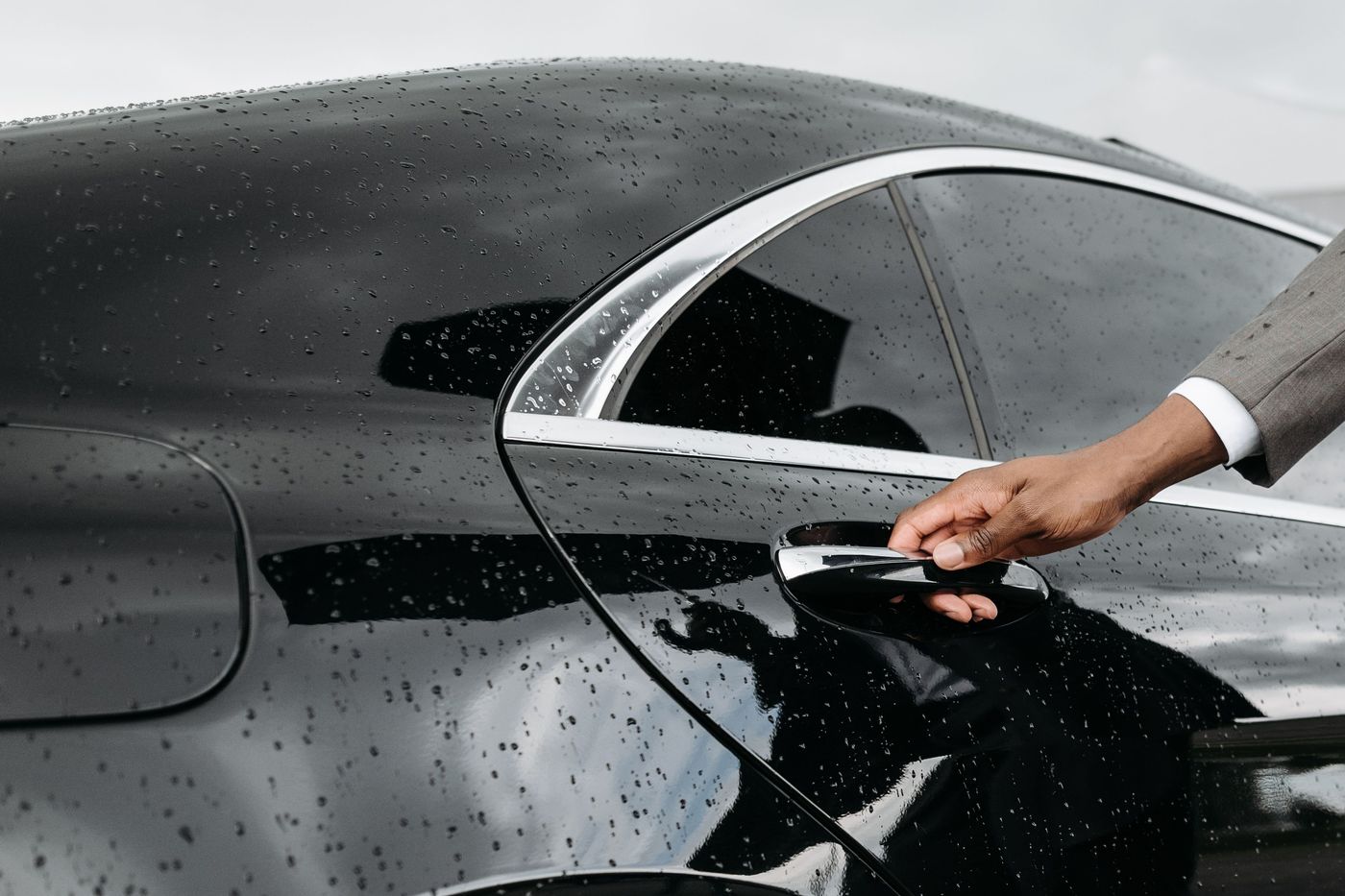 A suited chauffeur reaching for the door handle of a black sedan